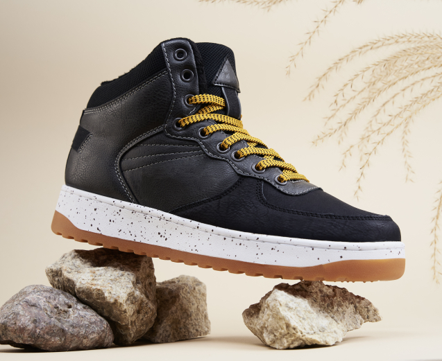 Male boots on beige background. Winter stylish leather shoes on stones with dried plant